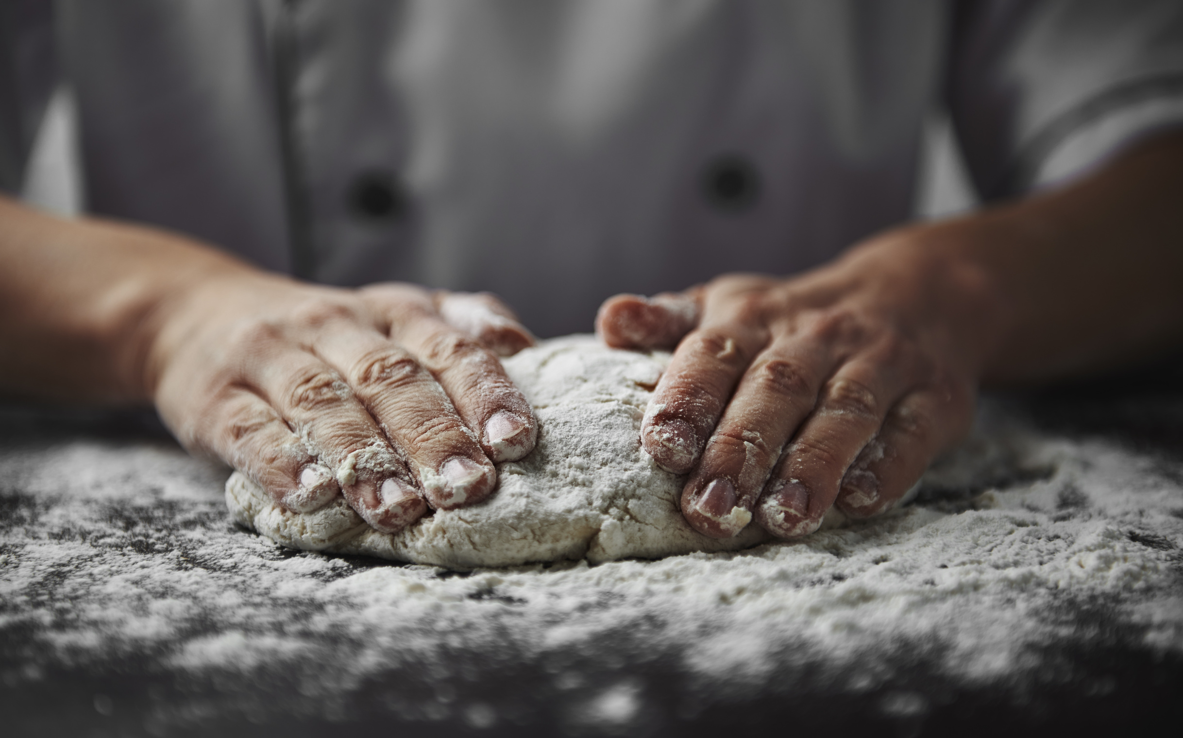 Close-up of woman baker hands kneading the dough on black board with flour powder. Concept of baking and patisserie. Close-up of woman baker hands kneading the dough on black board with flour powder. Concept of baking and patisserie.